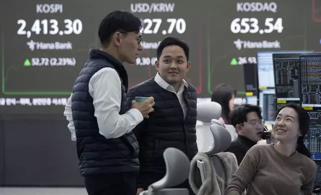 Currency traders smile near a screen showing the Korea Composite Stock Price Index (KOSPI), top left, and the foreign exchange rate between U.S. dollar and South Korean won, top center, at the foreign exchange dealing room of the KEB Hana Bank headquarters in Seoul, South Korea, Tuesday, Dec. 10, 2024. (AP Photo/Ahn Young-joon)