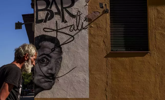 FILE - A man walks past a drawing representing the Spanish surrealist artist Salvador Dali during a hot and sunny day in Madrid, Spain, Thursday, July 13, 2023. (AP Photo/Manu Fernandez, File)