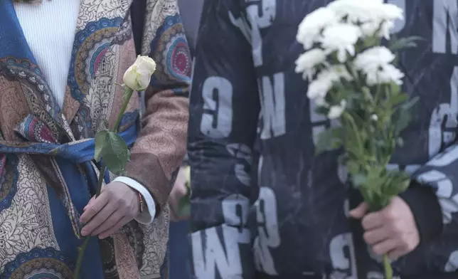 Students hold white flowers in front of the court building during a verdict in trial of parents of a boy who killed 9 students and security guard in school shooting in 2023, in Belgrade, Serbia, Monday, Dec. 30, 2024. (AP Photo/Darko Vojinovic)