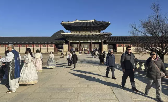 Tourists wearing traditional clothing rented from nearby shops pose for photos at the Gyeongbokgung Palace, in Seoul, Wednesday, Dec. 4, 2024. (AP Photo/ Jennifer McDermott)