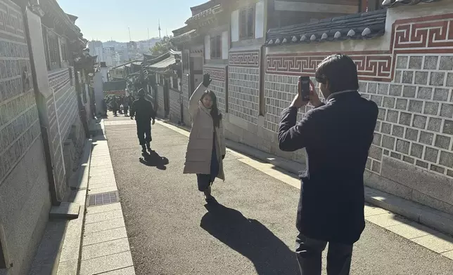 Tourists wander taking photos of the residential neighborhood and its many restored traditional houses in the Bukchon Hanok Village, in Seoul, Wednesday, Dec. 4, 2024. (AP Photo/ Jennifer McDermott)