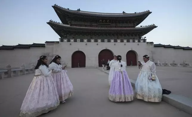 Jessica Hernandez, third from right, from the U.S. takes a photo near the Gwanghwamun, the main gate of the 14th-century Gyeongbok Palace, one of South Korea's well known landmarks, in Seoul, South Korea, Wednesday, Dec. 4, 2024. (AP Photo/Lee Jin-man)