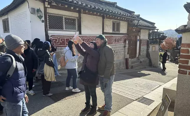 Tourists wander taking photos of the residential neighborhood and its many restored traditional houses in the Bukchon Hanok Village, in Seoul, Wednesday, Dec. 4, 2024. (AP Photo/ Jennifer McDermott)