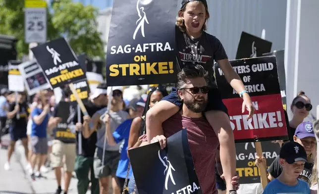 FILE - Director of Photography Jac Cheairs and his son, actor Wyatt Cheairs, 11, take part in a rally by striking writers and actors outside Netflix studio in Los Angeles on Friday, July 14, 2023. (AP Photo/Chris Pizzello, File)