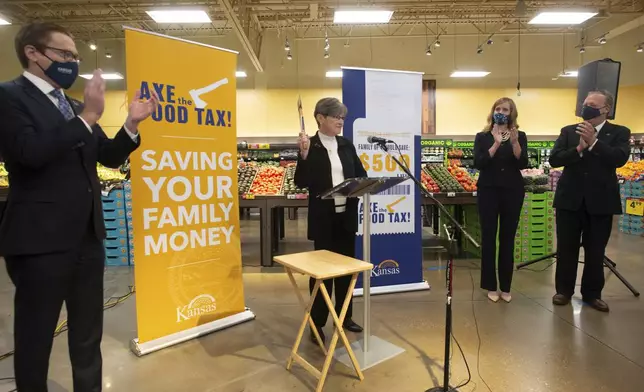 FILE - Surrounded by members of the legislature and signs touting saving families money, Kansas Gov. Laura Kelly announces her 'Axe the Food Tax' campaign at Dillons grocery store in Topeka, Kan., Monday, Nov. 8, 2021 by holding an axe. (Evert Nelson/The Capital-Journal via AP, File)