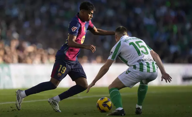 Barcelona's Lamine Yamal, left, challenges for the ball with Betis' Romain Perraud during a Spanish La Liga soccer match between Betis and Barcelona at the Benito Villamarin stadium in Seville, Spain, Saturday, Dec. 7, 2024. (AP Photo/Jose Breton)