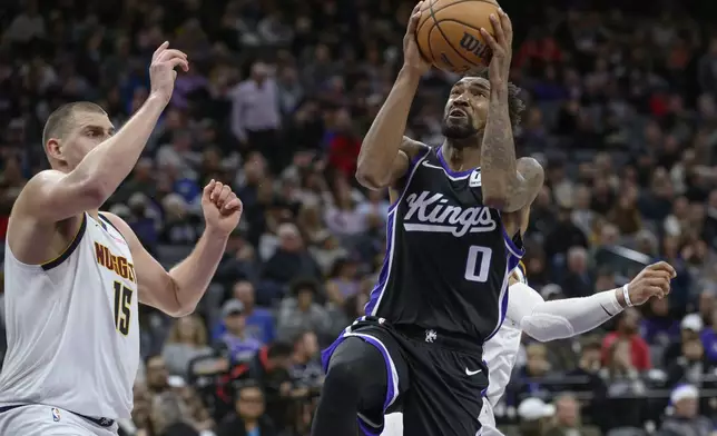 Sacramento Kings guard Malik Monk (0) drives to the basket past Denver Nuggets center Nikola Jokic (15) during the second half of an NBA basketball game in Sacramento, Calif., Monday, Dec. 16, 2024. The Nuggets won 130-129. (AP Photo/Randall Benton)