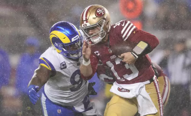 Rain falls as San Francisco 49ers quarterback Brock Purdy (13) tries to scramble before being sacked by Los Angeles Rams defensive tackle Kobie Turner, left, during the first half of an NFL football game in Santa Clara, Calif., Thursday, Dec. 12, 2024. (AP Photo/Godofredo A. Vásquez)