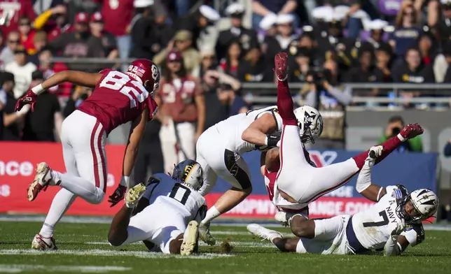 Oklahoma running back Gavin Sawchuk, second from right, is upended by Navy linebacker Mbiti Williams Jr. (7) and linebacker Kyle Jacob, center, during the first half of the Armed Forces Bowl NCAA college football game, Friday, Dec. 27, 2024, in Fort Worth, Texas. (AP Photo/Julio Cortez)