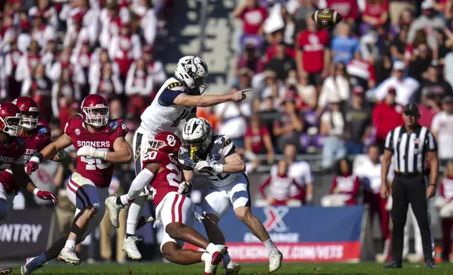 Navy quarterback Blake Horvath, top left, takes a hit from Oklahoma linebacker Lewis Carter (20) while attempting a pass during the first half of the Armed Forces Bowl NCAA college football game, Friday, Dec. 27, 2024, in Fort Worth, Texas. (AP Photo/Julio Cortez)