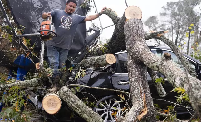 Saul Rodriguez uses a chain saw to remove debris atop a car from a woman's home after strong thunderstorms pass through the Greater Houston region, Saturday, Dec. 28, 2024, in Porter Heights. (Jason Fochtman/Houston Chronicle via AP)