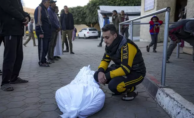 A man sits by the body of a Palestinian killed in the Israeli bombardment of the Gaza Strip at Al-Aqsa Hospital in Deir Al-Balah, Wednesday, Dec. 25, 2024. (AP Photo/Abdel Kareem Hana)