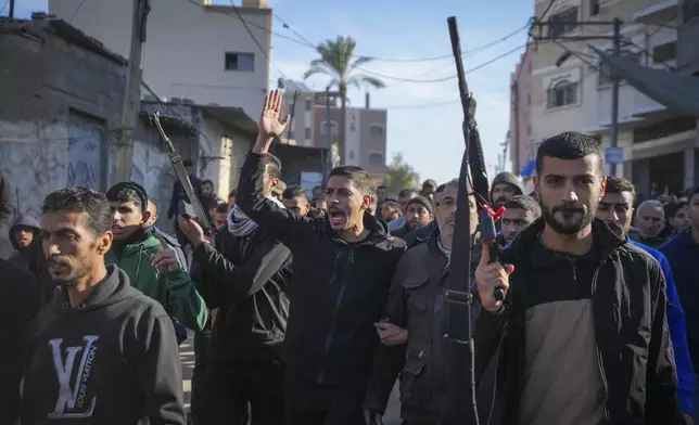 Relatives and neighbors, two of them holding guns, walk during the funeral procession of a victim of an Israeli strike on a home late Saturday that killed at least eight people, in Deir al-Balah, central Gaza Strip, Sunday, Dec. 22, 2024. Some families in Gaza are armed to protect their homes from thieves in the camps.(AP Photo/Abdel Kareem Hana)