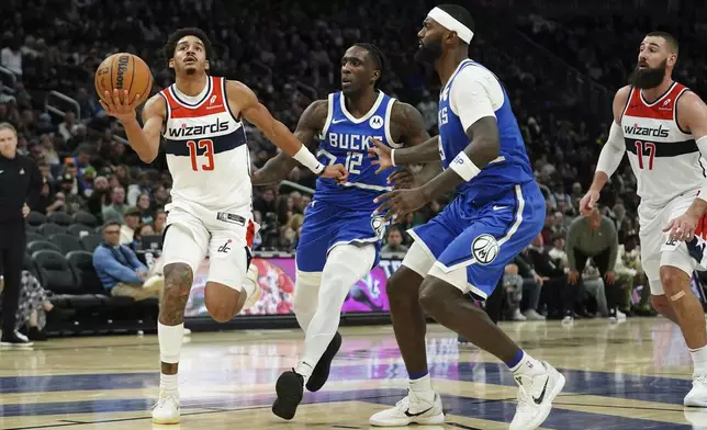 Washington Wizards' Jordan Poole (13) drives to the basket against Milwaukee Bucks' Taurean Prince (12) and Bobby Portis (9) during the first half of an NBA basketball game Saturday, Nov. 30, 2024, in Milwaukee. (AP Photo/Aaron Gash)