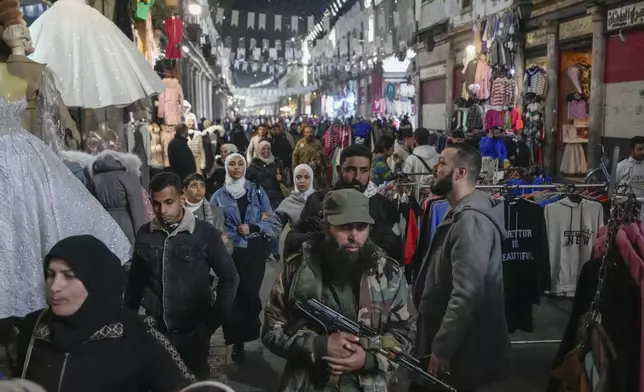 FILE - An armed opposition fighter walks among costumers at the Al-Hamidiyeh market inside the old walled city of Damascus, Syria, Tuesday, Dec. 10, 2024. (AP Photo/Hussein Malla, File)