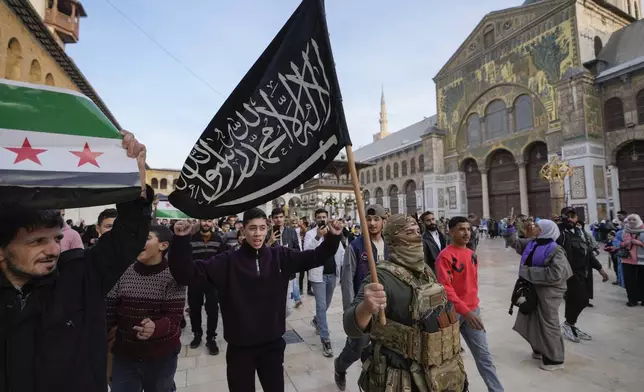 FILE - A masked opposition fighter carries a flag of Hayat Tahrir al-Sham (HTS) in the courtyard of the Umayyad Mosque in the old walled city of Damascus, Syria, on Tuesday, Dec. 10, 2024. HTS is the largest rebel faction within the opposition that toppled Bashar Assad's regime last Sunday. (AP Photo/Hussein Malla, File)