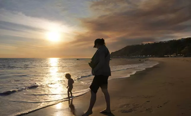 Malibu residents Florence Johnson and her son Brian enjoy the beach before sunset as a plume of smoke from the Franklin Fire rises over the ocean Tuesday, Dec. 10, 2024, in Malibu, Calif. (AP Photo/Damian Dovarganes)