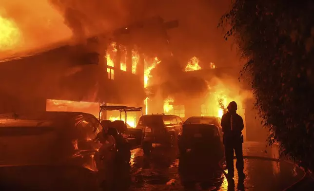 A firefighter sprays water on a home as it burns in the Franklin Fire in Malibu, Calif., Tuesday, Dec. 10, 2024. (AP Photo/Jae C. Hong)