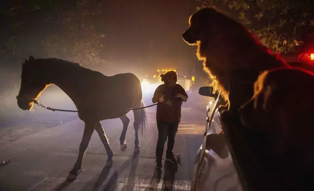 A woman evacuates a horse as the Franklin Fire burns in Malibu, Calif., on Tuesday, Dec. 10, 2024. (AP Photo/Ethan Swope)