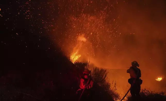 Two firefighters put out flames while battling the Franklin Fire in Malibu, Calif., Tuesday, Dec. 10, 2024. (AP Photo/Jae C. Hong)