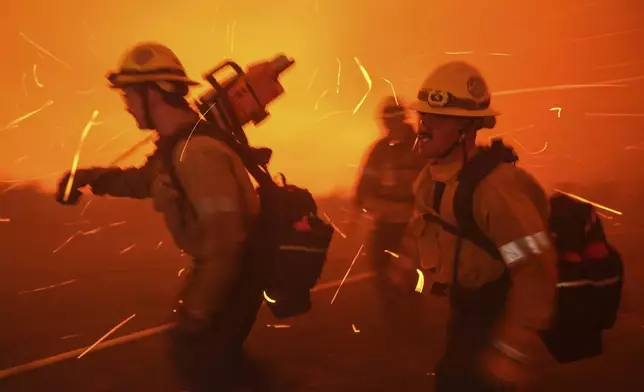 Firefighters are pushed back by gusty winds while removing fuel around the faculty and staff residences at Pepperdine University as the Franklin Fire approaches in Malibu, Calif., Tuesday, Dec. 10, 2024. (AP Photo/Jae C. Hong)