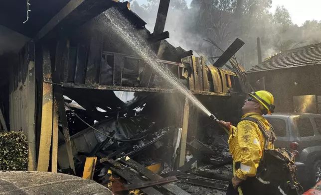 A firefighter hoses down hot spots around a fire-ravaged property after the Franklin Fire swept through Tuesday, Dec. 10, 2024, in Malibu, Calif. (AP Photo/Eugene Garcia)