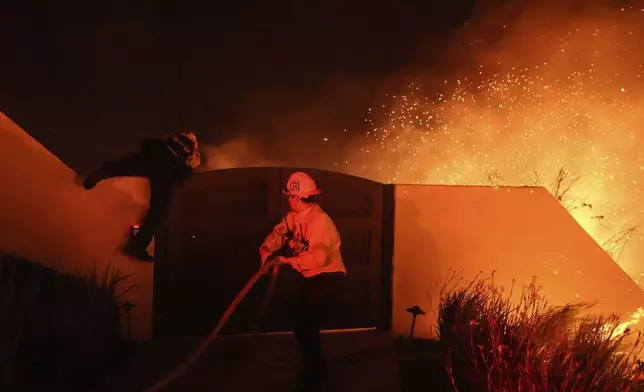 Embers fly in gusty winds as two Los Angeles County firefighters battle the Franklin Fire at Pepperdine University in Malibu, Calif., Tuesday, Dec. 10, 2024. (AP Photo/Jae C. Hong)