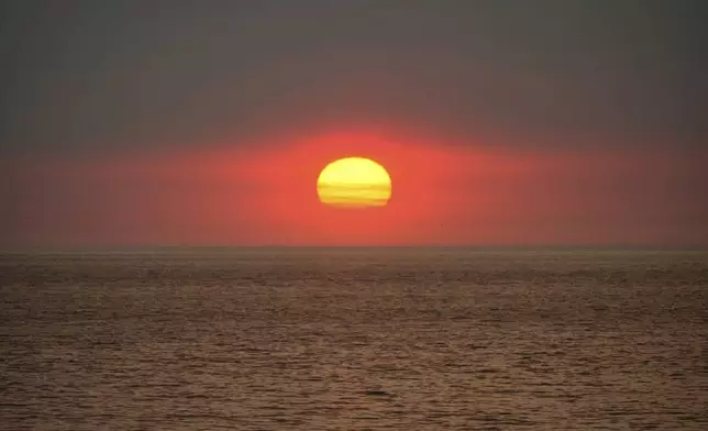 The sun sets under a plume of smoke from the Franklin Fire rising over the ocean Tuesday, Dec. 10, 2024, in Malibu, Calif. (AP Photo/Damian Dovarganes)