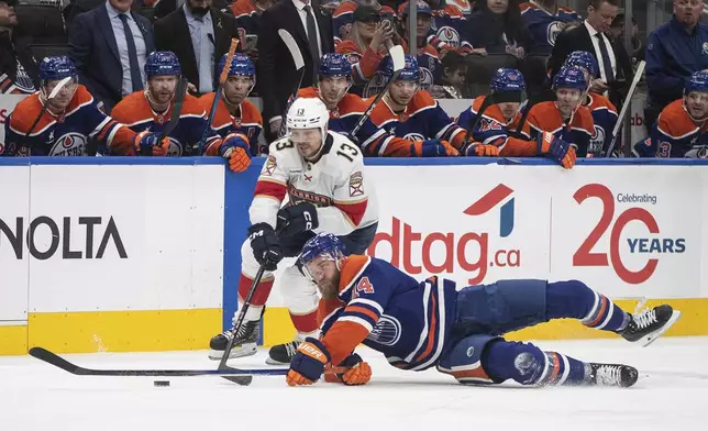 Florida Panthers' Sam Reinhart (13) and Edmonton Oilers' Mattias Ekholm (14) battle for the puck during third-period NHL hockey game action in Edmonton, Alberta, Monday, Dec. 16, 2024. (Jason Franson/The Canadian Press via AP)