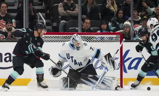 Utah Hockey Club goaltender Karel Vejmelka (70) deflects a shot from Seattle Kraken center Jaden Schwartz, left, during the first period of an NHL hockey game Monday, Dec. 30, 2024, in Seattle. (AP Photo/Lindsey Wasson)