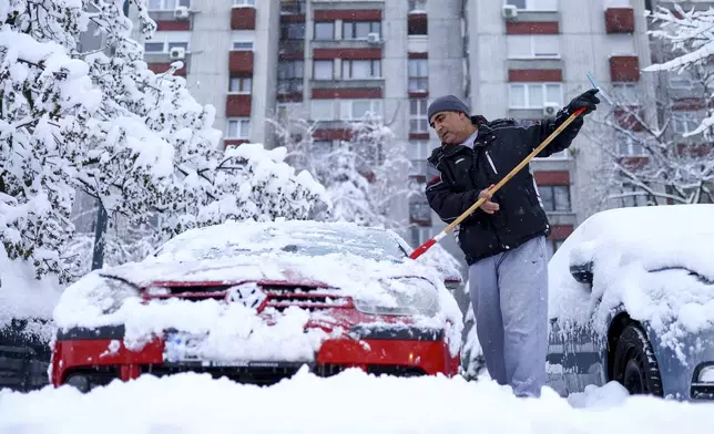 A man cleans snow of his car during heavy snowfall in Sarajevo, Bosnia, Tuesday, Dec. 24, 2024. (AP Photo/Armin Durgut)