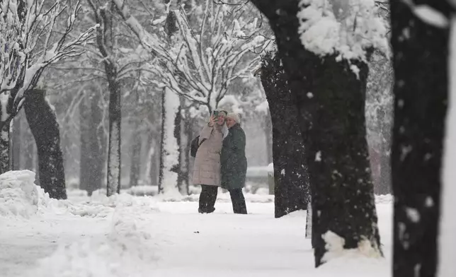 Two women take a selfie in a snow covered park during a snowfall, in Belgrade, Serbia, Tuesday, Dec. 24, 2024. (AP Photo/Darko Vojinovic)