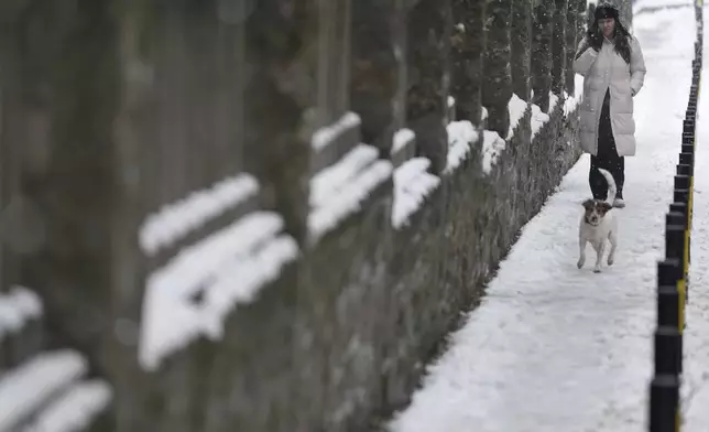 A woman with a dog walks through a snow covered street in Belgrade, Serbia, Tuesday, Dec. 24, 2024. (AP Photo/Darko Vojinovic)