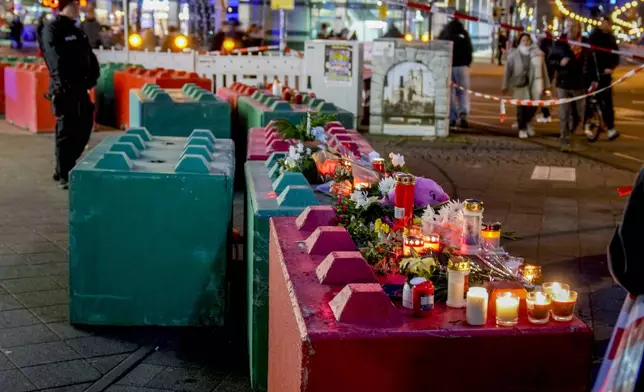 People lay flowers and light candles on concrete blocks that protect the Christmas market, where a car drove into a crowd on Friday evening, in Magdeburg, Germany, Saturday, Dec. 21, 2024. (AP Photo/Michael Probst)