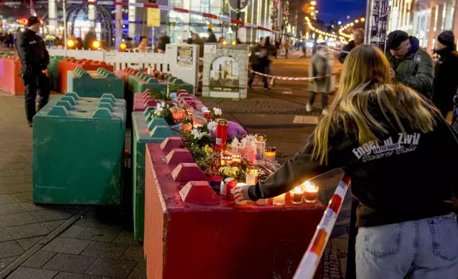 People lay flowers and light candles on concrete blocks that protect the Christmas market in Magdeburg, Germany, Saturday, Dec. 21, 2024, where a car drove into a crowd on Friday evening. (AP Photo/Michael Probst)