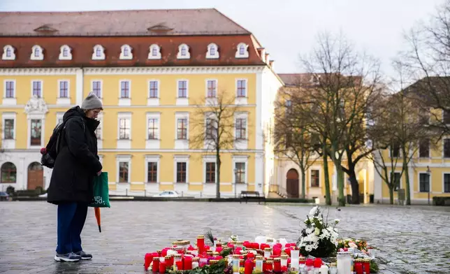 A woman stands next to flowers and candles laid down near the Magdeburg Cathedral, after a car drove into a crowd of a Christmas Mark on Friday evening, in Magdeburg, Germany, Sunday, Dec. 22, 2024. (AP Photo/Ebrahim Noroozi)