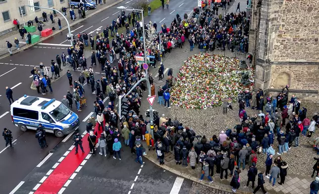 People gather to lay flowers and light candles at the entrance of Johannis church near the Christmas Market, where a car drove into a crowd on Friday evening, in Magdeburg, Germany, Sunday, Dec. 22, 2024. (AP Photo/Michael Probst)