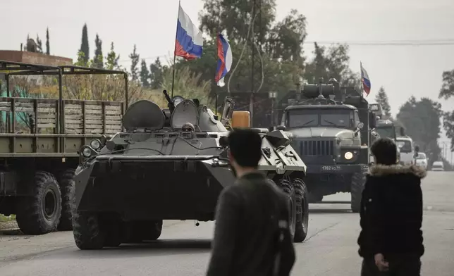 Syrian fighters watch Russian armoured vehicles driving past near the Hmeimim Air Base, a Syrian airbase currently operated by Russia, in the town of Hmeimim, southeast of Latakia, Syria, Monday Dec. 16, 2024.(AP Photo/Leo Correa)