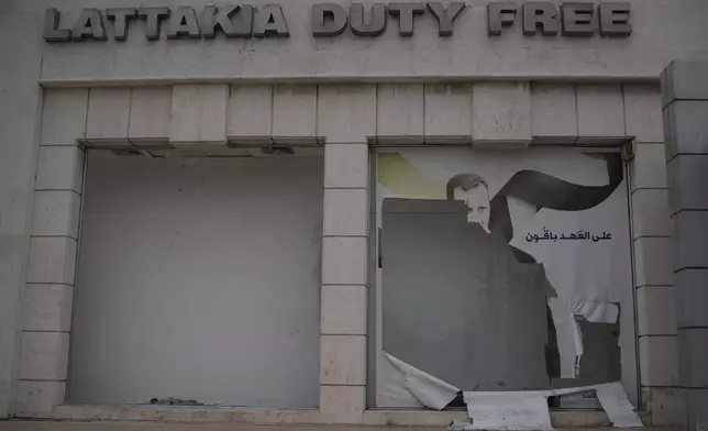 A damaged shop window with an image depicting Bashar Assad is seen at the port of Latakia, Syria, Monday, Dec. 16, 2024. (AP Photo/Leo Correa)