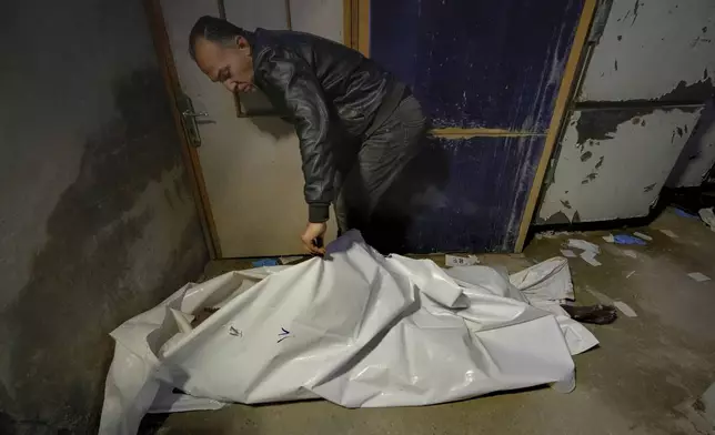 A man examines a body wrapped in a plastic bag at the Al-Mojtahed Hospital in Damascus, Syria, on Wednesday, Dec. 11, 2024. Many are flocking to morgues, hoping to identify loved ones who have been killed or were imprisoned under the rule of President Bashar Assad, whose government collapsed over the weekend. (AP Photo/Hussein Malla)