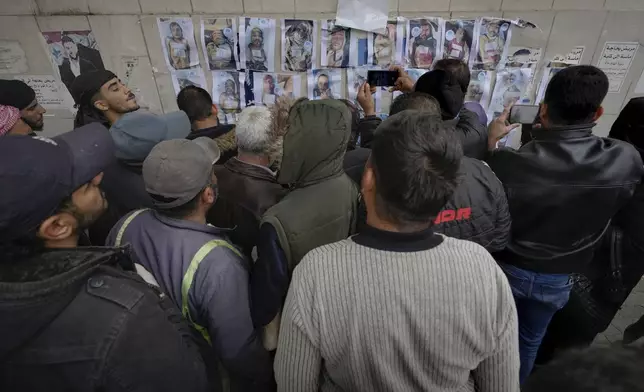 People examine photos as they search for missing or deceased people on the wall outside the morgue of Al-Mojtahed Hospital in Damascus, Syria, on Wednesday, Dec. 11, 2024. Many are flocking to morgues, hoping to identify loved ones who have been killed or were imprisoned under the rule of President Bashar Assad, whose government collapsed over the weekend. (AP Photo/Hussein Malla)