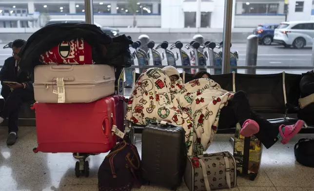 Two travelers nap near the Alaska Airlines ticketing area at the Los Angeles International Airport in Los Angeles, Tuesday, Dec. 24, 2024. (AP Photo/Jae C. Hong)