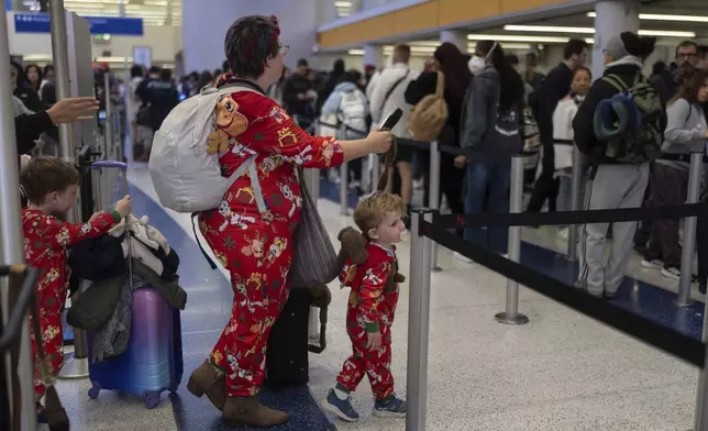 Marie Digna, traveling to Grand Rapids, Mich., enters security with her two sons, Lucian, right, and Samson, at Los Angeles International Airport on Tuesday, Dec. 24, 2024. (AP Photo/Jae C. Hong)