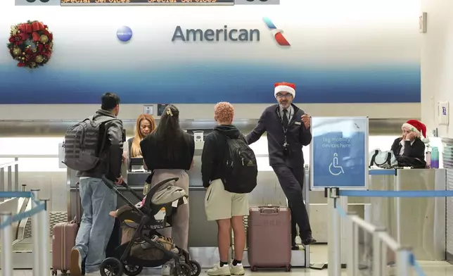 American Airlines employees, some wearing Santa Claus hats, check in travelers in the American terminal at Miami International Airport, on Christmas Eve, Tuesday, Dec. 24, 2024, in Miami. (AP Photo/Rebecca Blackwell)