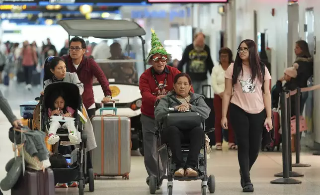 Cesar Davila, who works for the American Airlines partner providing wheelchair assistance, wears a Christmas tree hat and festive glasses as he pushes a traveler through the American Airlines terminal at Miami International Airport, on Christmas Eve, Tuesday, Dec. 24, 2024, in Miami. (AP Photo/Rebecca Blackwell)