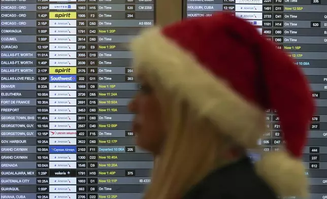 An employee wearing a Santa Claus hat walks past boards showing flight delays, in the American Airlines terminal at Miami International Airport, on Christmas Eve, Tuesday, Dec. 24, 2024, in Miami. (AP Photo/Rebecca Blackwell)