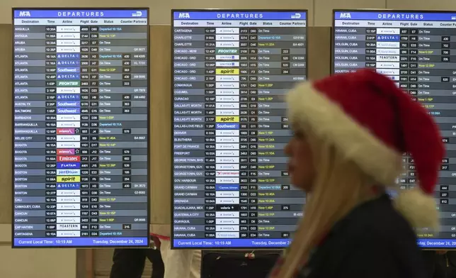 An employee wearing a Santa Claus hat walks past boards showing flight delays, in the American Airlines terminal at Miami International Airport, on Christmas Eve, Tuesday, Dec. 24, 2024, in Miami. (AP Photo/Rebecca Blackwell)