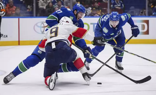 Vancouver Canucks' Derek Forbort (27) and Florida Panthers' Sam Bennett (9) collide as Canucks' Tyler Myers (57) watches during the second period of an NHL hockey game in Vancouver, British Columbia, Thursday, Dec. 12, 2024. (Darryl Dyck/The Canadian Press via AP)