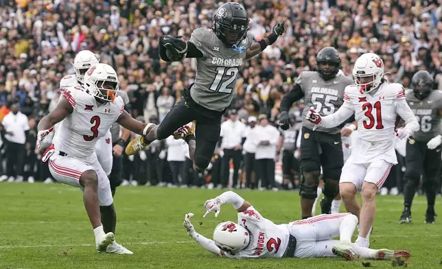 FILE - Colorado wide receiver Travis Hunter (12) flies in for a touchdown past, from left, Utah linebacker Johnathan Hall, cornerback Smith Snowden and safety Nate Ritchie during the second half of an NCAA college football game Saturday, Nov. 16, 2024, in Boulder, Colo. (AP Photo/David Zalubowski, File)