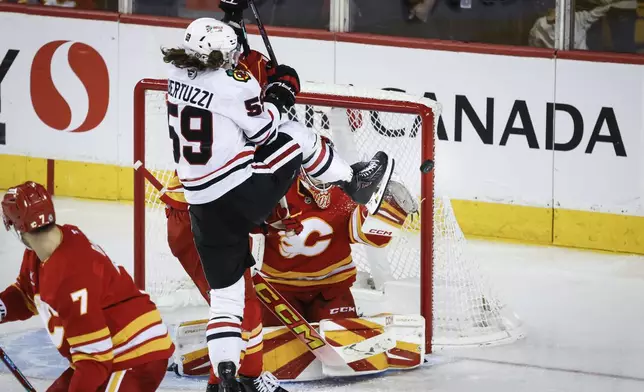 Chicago Blackhawks' Tyler Bertuzzi, left, deflects the puck off his skate as Calgary Flames goalie Dustin Wolf guards the net during the third period of an NHL hockey game in Calgary, Alberta, on Saturday, Dec. 21, 2024. (Jeff McIntosh/The Canadian Press via AP)